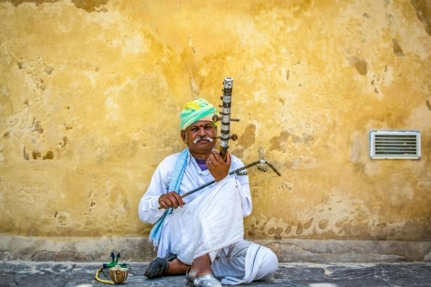 Rajasthani musician playing a ravanahatha against a yellow wall